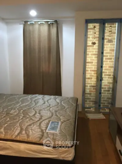 Cozy bedroom with natural light and wooden flooring, featuring a comfortable bed and window view.