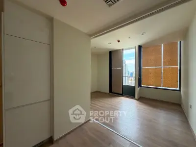 Spacious modern room with wooden flooring and large windows offering city views.