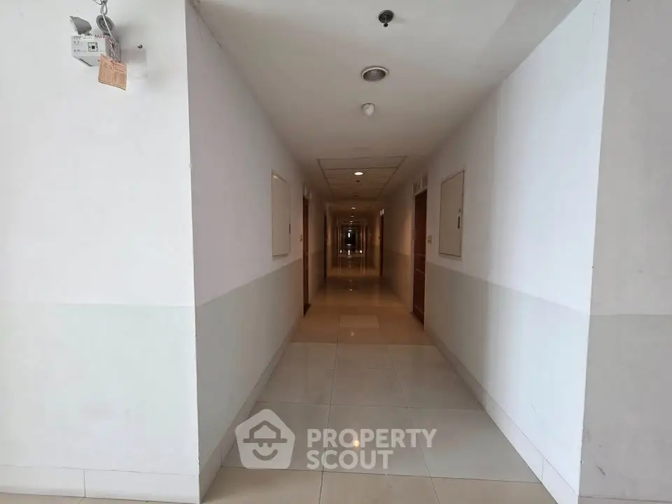 Spacious and well-lit hallway in modern apartment building with tiled flooring.