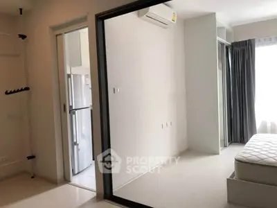 Modern minimalist bedroom with sliding glass door and air conditioning, adjacent to a sleek kitchen area.