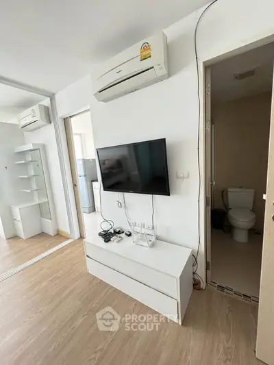Modern living room with air conditioning and wall-mounted TV, adjacent to a compact bathroom.