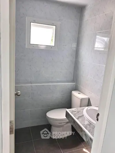 Compact bathroom with modern fixtures and tiled walls, featuring a small window for natural light.