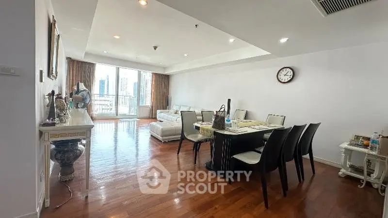 Spacious living and dining area with city view, featuring elegant decor and hardwood floors.
