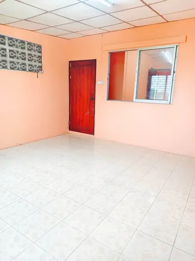 Spacious empty room with tiled floor and peach walls, featuring a wooden door and large window.