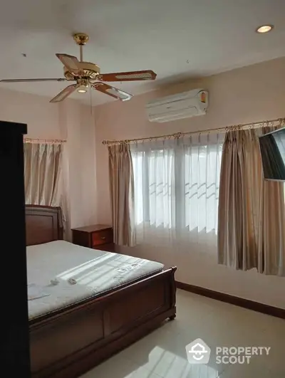 Spacious bedroom with elegant wooden furniture and ceiling fan, featuring large windows for natural light.