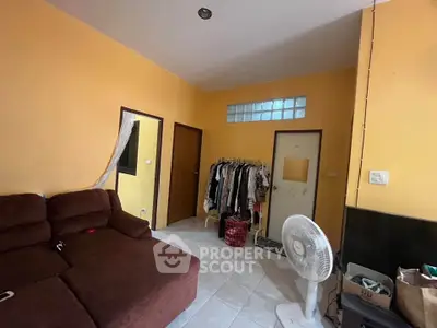 Cozy living room with brown sofa, fan, and clothing rack in a warm yellow painted space.