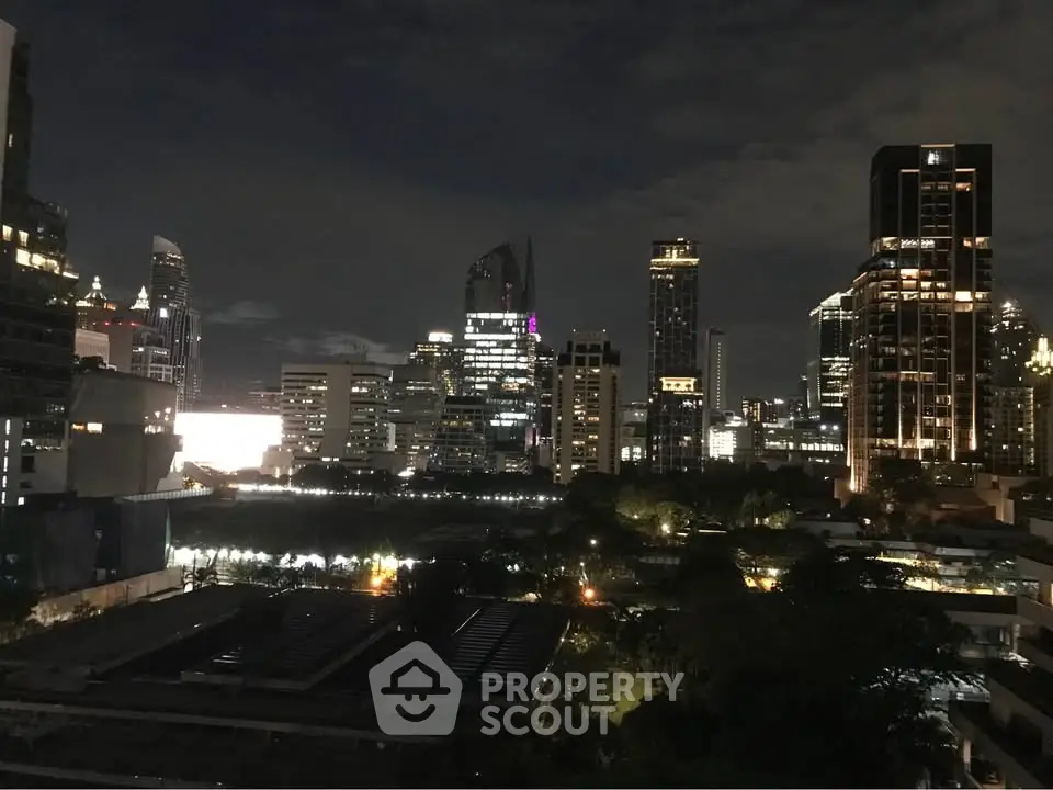 Stunning city skyline view at night with illuminated skyscrapers and lush greenery.