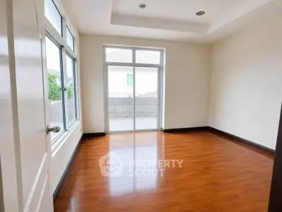Spacious empty room with wooden flooring and large windows leading to a balcony.