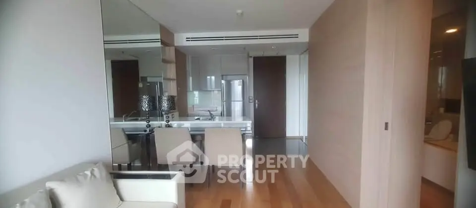 Modern open-plan living room with sleek kitchen and dining area, featuring elegant furniture and wooden flooring.