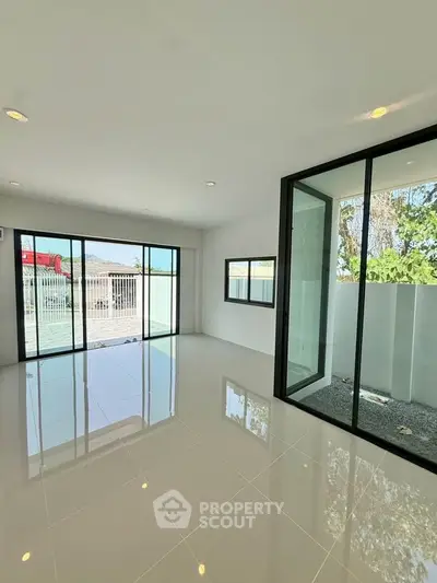 Spacious modern living room with large windows and glossy tile flooring, offering abundant natural light and garden view.