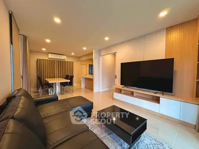 Spacious modern living room with sleek black leather sofa and large flat-screen TV, perfect for relaxation.