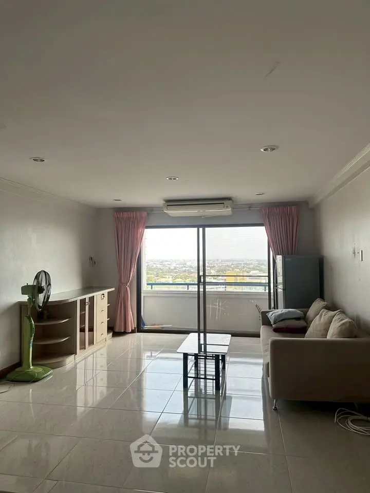 Spacious living room with large window offering stunning city views, featuring modern furniture and tiled flooring.