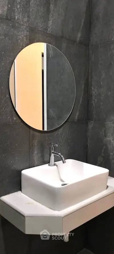 Modern bathroom with sleek sink and round mirror on dark tiled wall.
