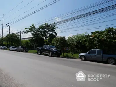 Spacious roadside view with greenery and parked cars, ideal for urban development.