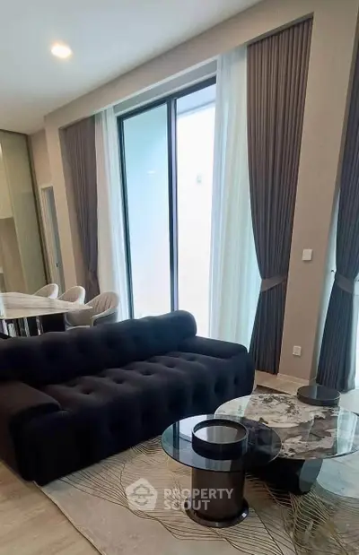 Modern living room with elegant black sofa, marble coffee table, and floor-to-ceiling windows with stylish curtains.