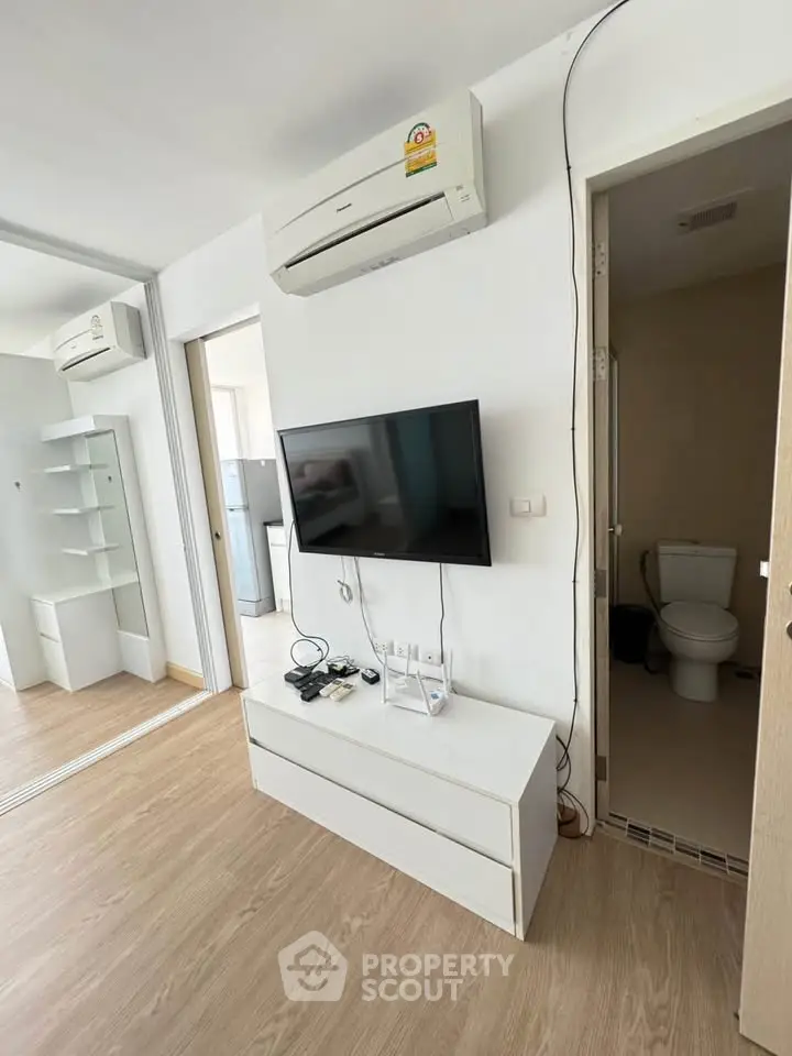 Modern living room with air conditioning and wall-mounted TV, adjacent to a compact bathroom.