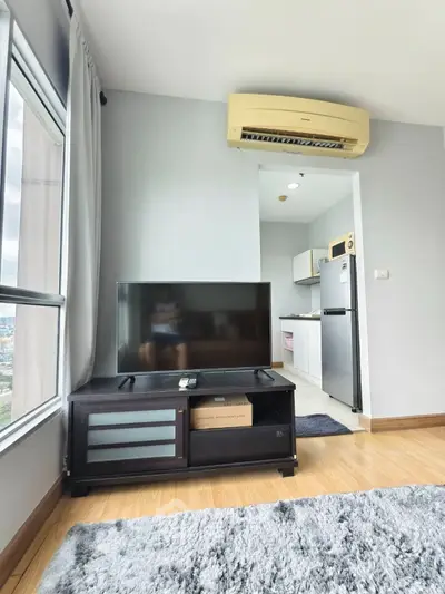 Modern living room with TV and kitchen view, featuring sleek design and natural light.