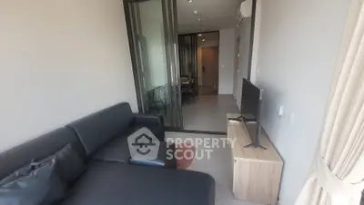 Modern living room with sleek black sofa and flat-screen TV, featuring glass partition and stylish decor.