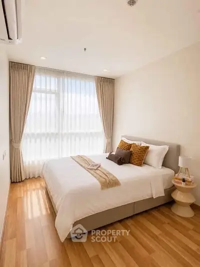 Cozy and bright bedroom with wooden flooring and large window, perfect for relaxation.