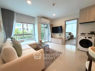 Modern living room with cozy sofa, TV, and washing machine, leading to a bright bedroom with large windows.