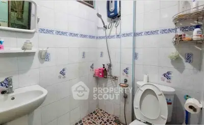 Compact bathroom with shower, sink, and toilet in a tiled setting, featuring wall-mounted storage.