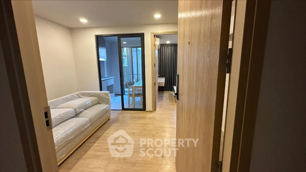 Spacious and modern living room with gleaming hardwood floors and large glass doors leading to a sunlit balcony, perfect for entertaining or relaxation.