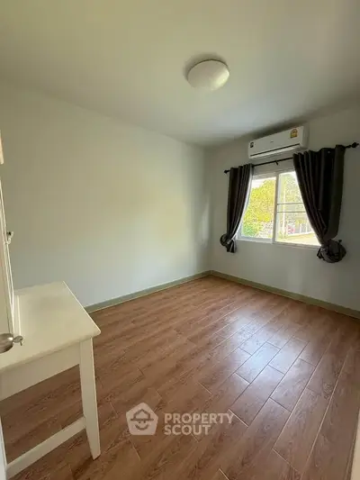 Spacious bedroom with wooden flooring and natural light from window