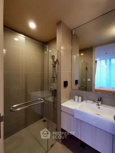 Modern bathroom with glass shower and sleek vanity in contemporary apartment.