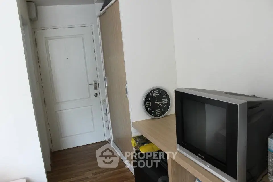 Compact apartment interior with wooden flooring, TV, and wall clock near entrance door.