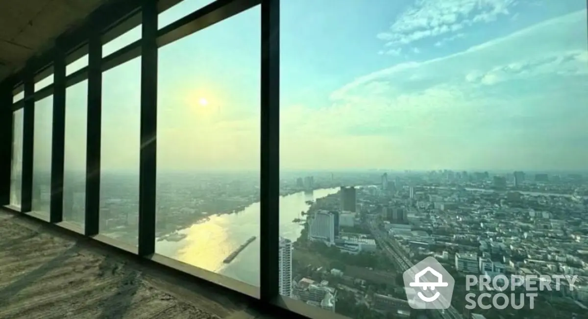 Stunning high-rise view of cityscape and river at sunset from floor-to-ceiling windows.