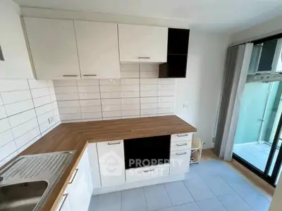 Modern kitchen with sleek white cabinets and wooden countertops, featuring a tiled backsplash and ample natural light.