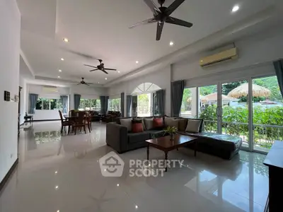 Spacious open-plan living room with large windows and garden view, featuring modern furniture and ceiling fans.