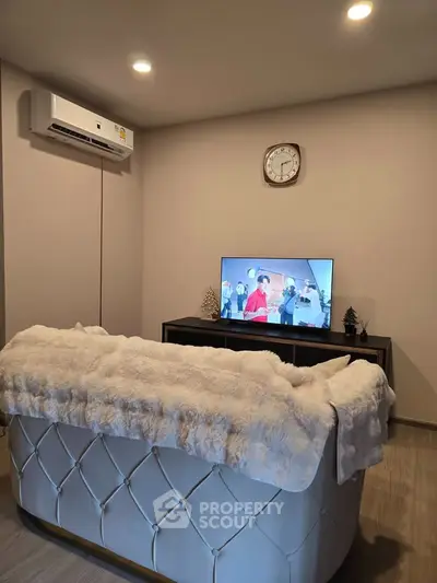 Cozy living room with plush sofa, wall-mounted TV, and modern air conditioning unit.