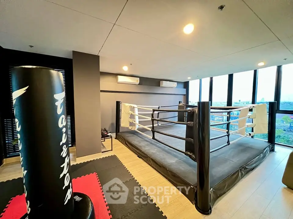 Modern gym with boxing ring and punching bag, featuring city views.