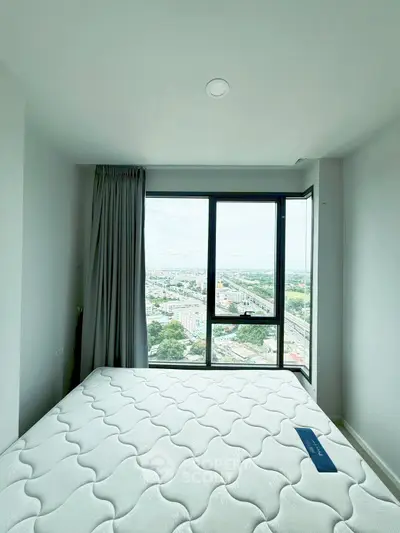 Bright bedroom with large window offering stunning city view, featuring a comfortable mattress and modern design.