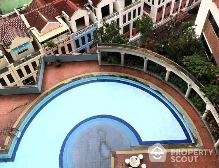 Aerial view of a serene communal pool surrounded by a terracotta-tiled patio and lush greenery, nestled within a charming residential complex.