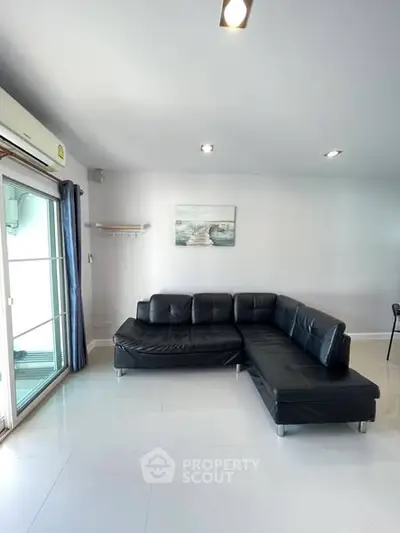 Spacious living room with modern black leather sectional sofa and large window for natural light.