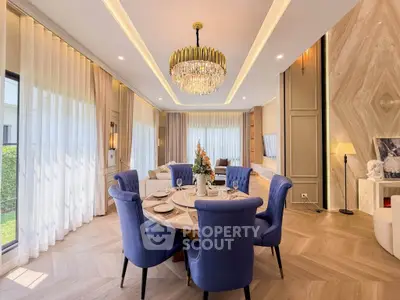 Luxurious dining area with elegant chandelier and plush blue chairs in a modern open-layout living space.