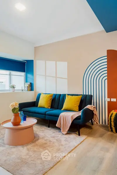 Stylish living room with modern decor, featuring a blue sofa, colorful cushions, and geometric wall art.