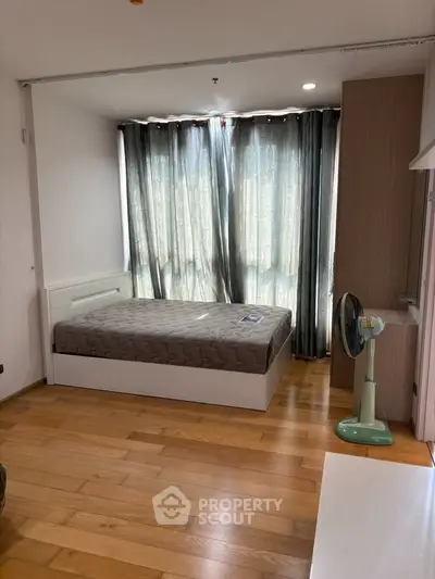 Spacious bedroom with wooden flooring and large windows for natural light.