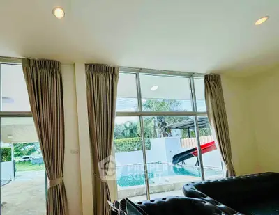 Spacious living room with pool view through large windows and elegant curtains.