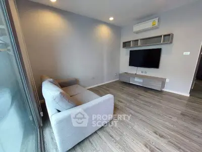 Modern living room with sleek wooden flooring and minimalist furniture, featuring a wall-mounted TV and air conditioning.