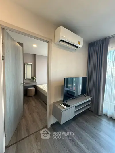 Modern living room with TV and air conditioning, leading to a cozy bedroom with natural light.