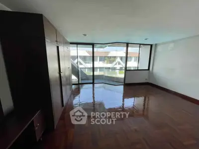 Spacious room with large windows and polished wooden floors, offering a bright and airy atmosphere.