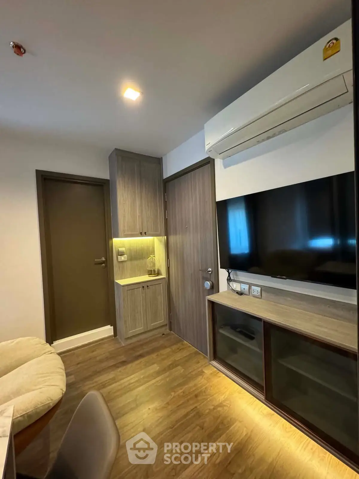Modern living room with wooden flooring, wall-mounted TV, and air conditioning unit.