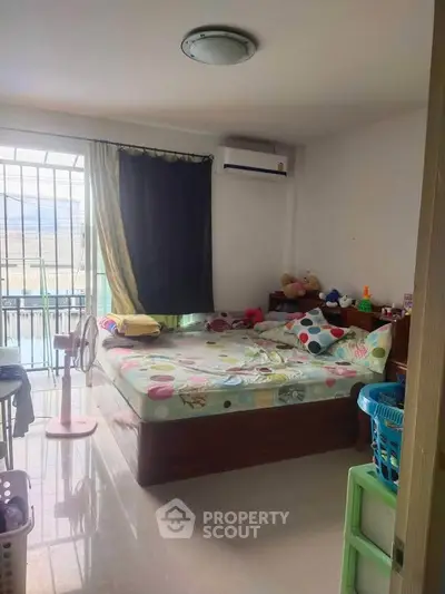 Cozy bedroom with colorful bedding and natural light, featuring air conditioning and a view of the balcony.