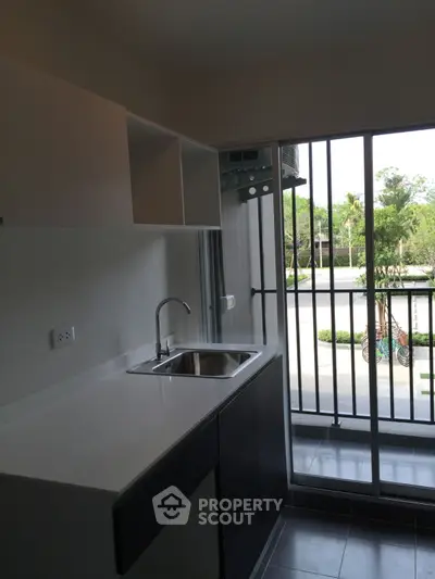 Modern kitchen with sleek design and balcony view, featuring a stainless steel sink and ample storage.