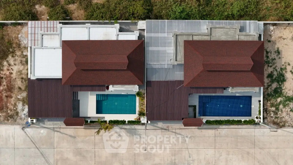 Aerial view of two modern villas with private pools and red roofs, showcasing luxury real estate.