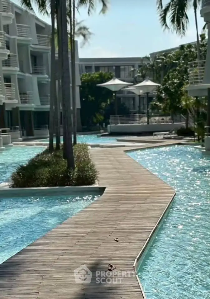 Luxurious resort-style pool area with wooden walkway and palm trees, perfect for relaxation and leisure.