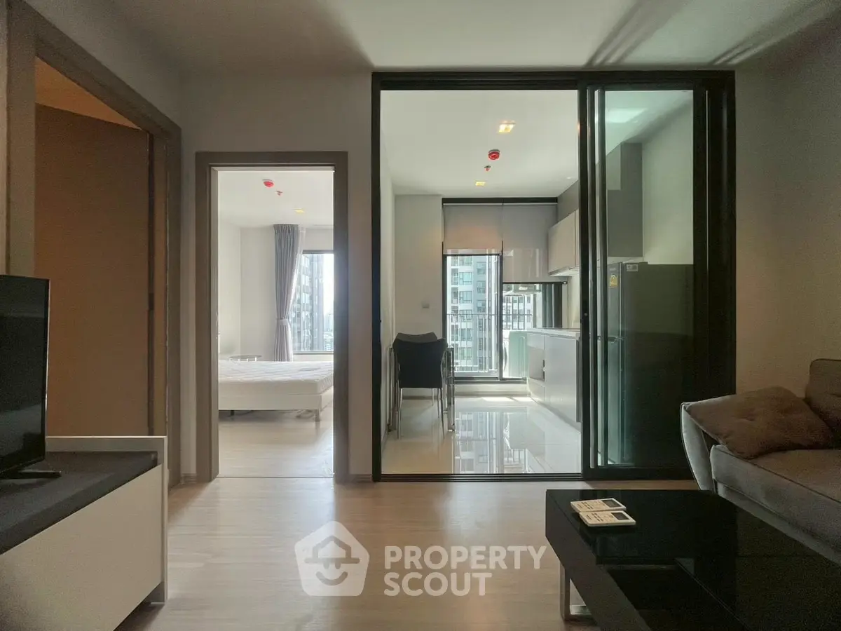 Modern apartment interior with open layout, featuring living room, kitchen, and bedroom view.